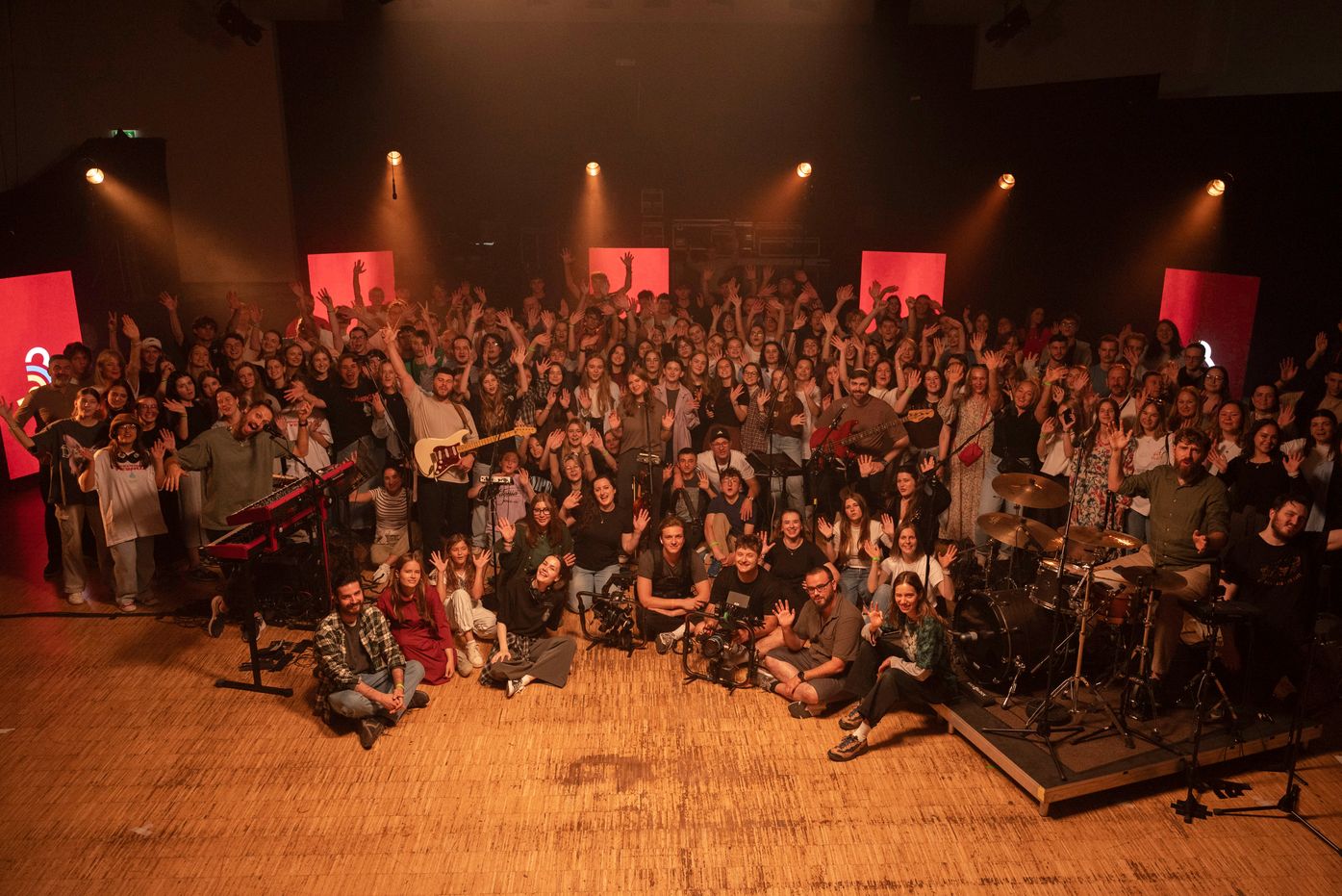 Large youth crowd on stage with their hands raised at GFWeekend, warm red stage lights
