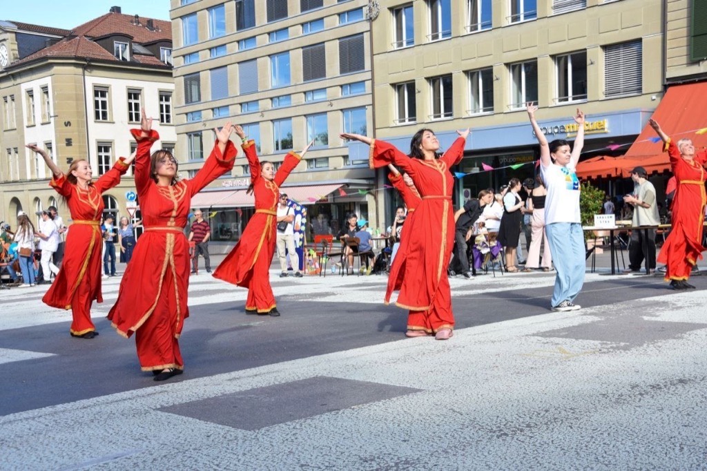 Group of women in red traditional robes performing a dance in a public square